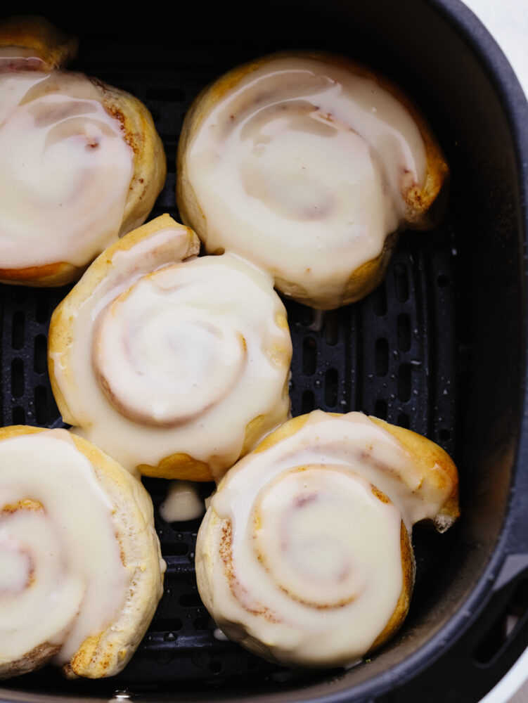 Cinnamon rolls in a air fryer basket with frosting. 