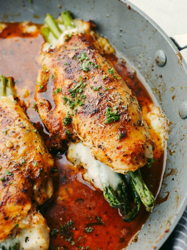 A close up of a pan with a chicken breast stuffed with cheese and asparagus. 