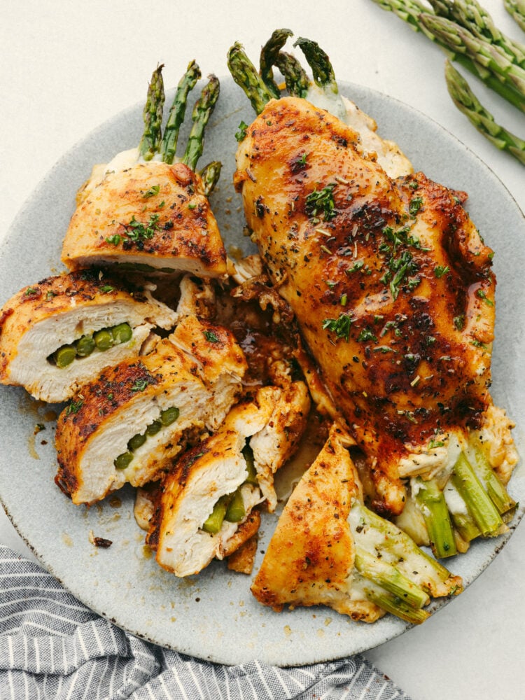 A gray plate with one whole asparagus stuffed chicken breast and another breast that is sliced into 5 pieces. 