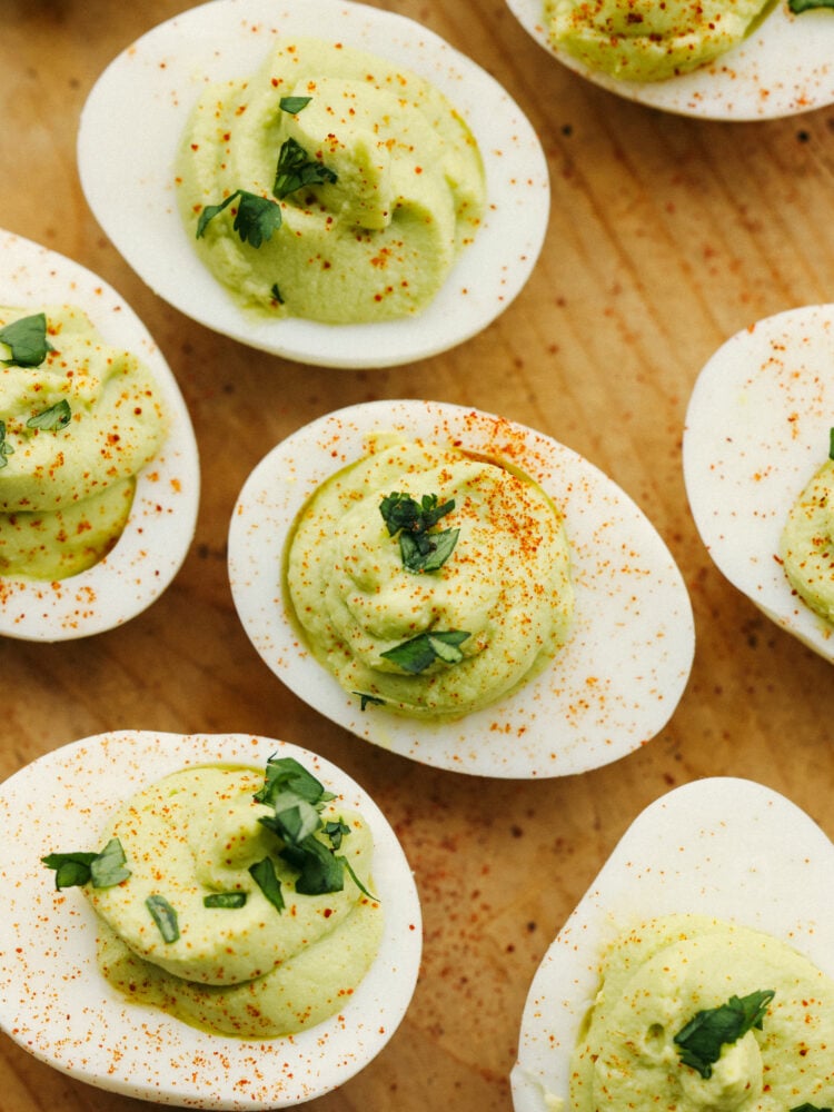 Avocado deviled eggs on a wooden board, dusted with paprika.