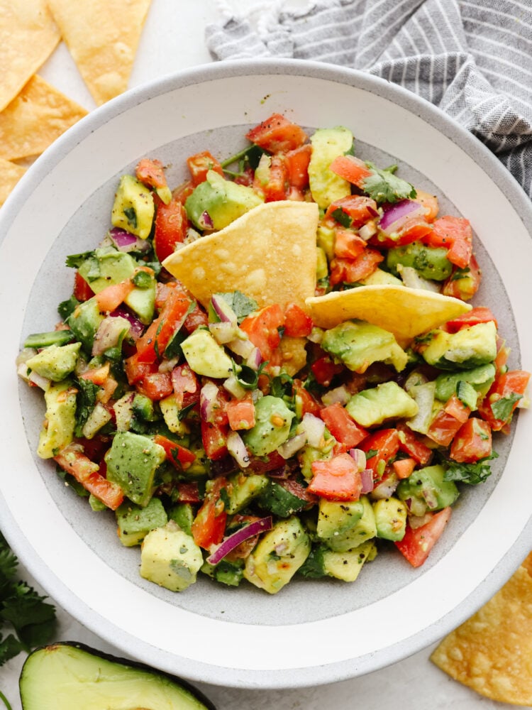A bowl of avocado salsa with tortilla chips  dipped in it. 