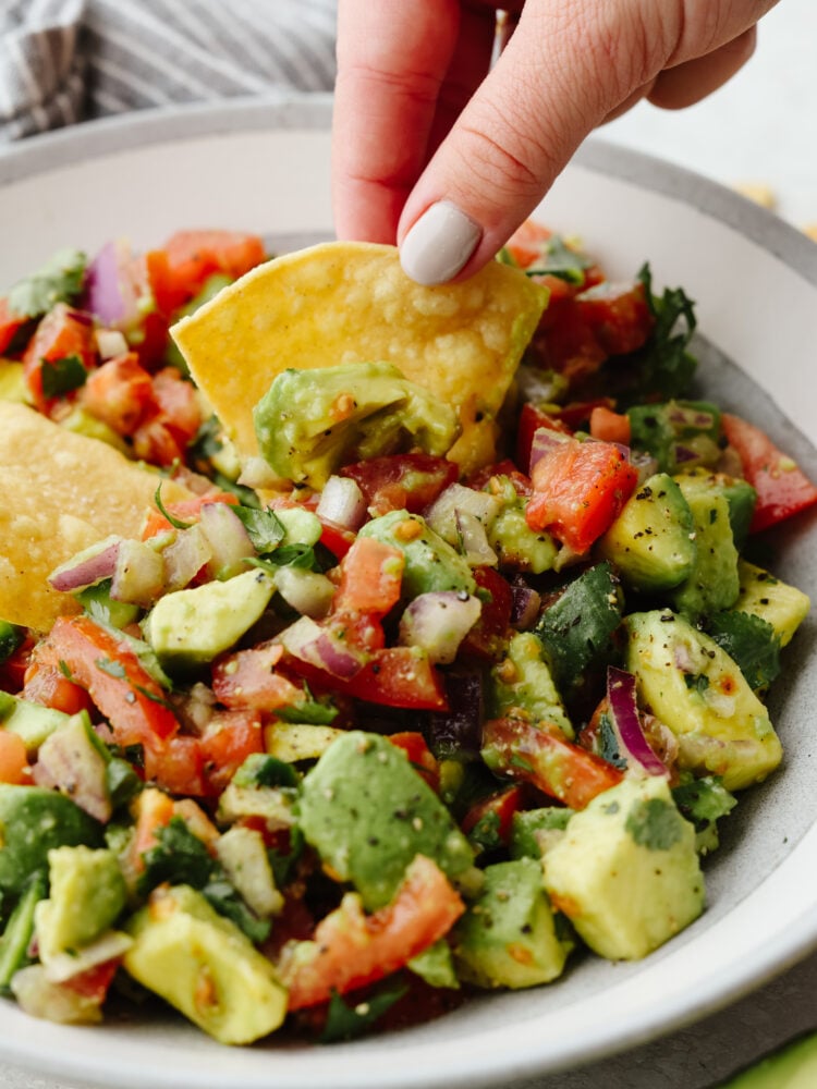 A tortilla chip being dipped into avocado salsa. 