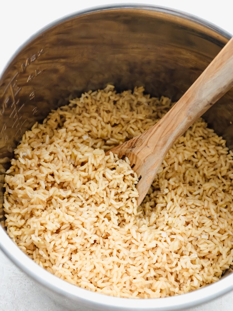 Hero image of brown rice in an Instant Pot, being stirred with a wooden spoon.