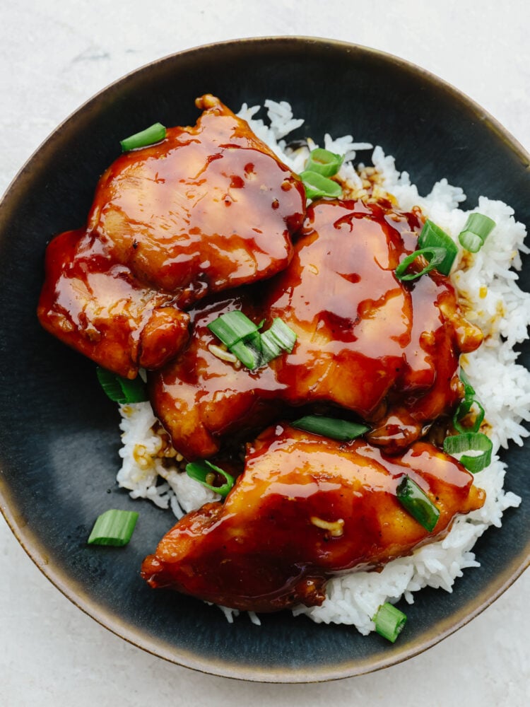 Caramel chicken served over white rice in a black bowl.