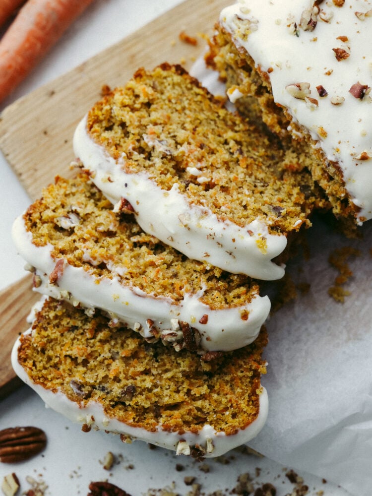 A loaf of carrot cake bread on a wooden cutting board sliced with a glaze on top. 