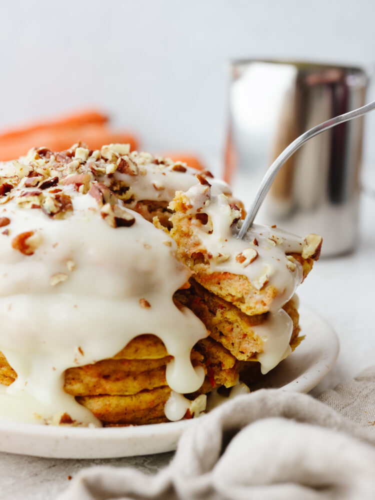 A stack of carrot cake pancakes with a carrot cake glaze with a fork cutting into them.