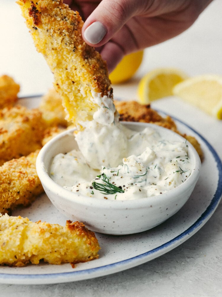 A fish stick being dipped in tartar sauce. 