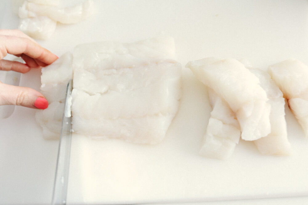 A picture of cod on a cutting board being cut into slices. 
