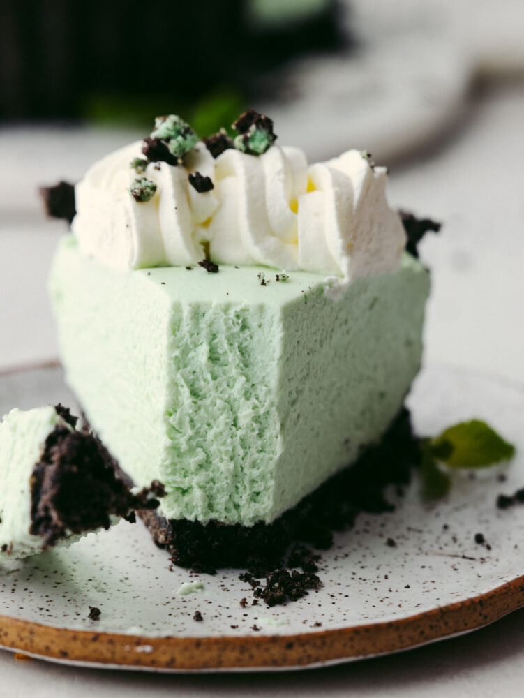 A slice of grasshopper pie on a plate with a bite cute out of the tip of the slice. 