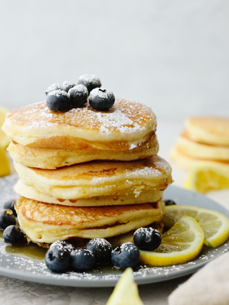 A stack of lemon ricotta pancakes on a gray plate that are topped with blueberries and powdered sugar. 