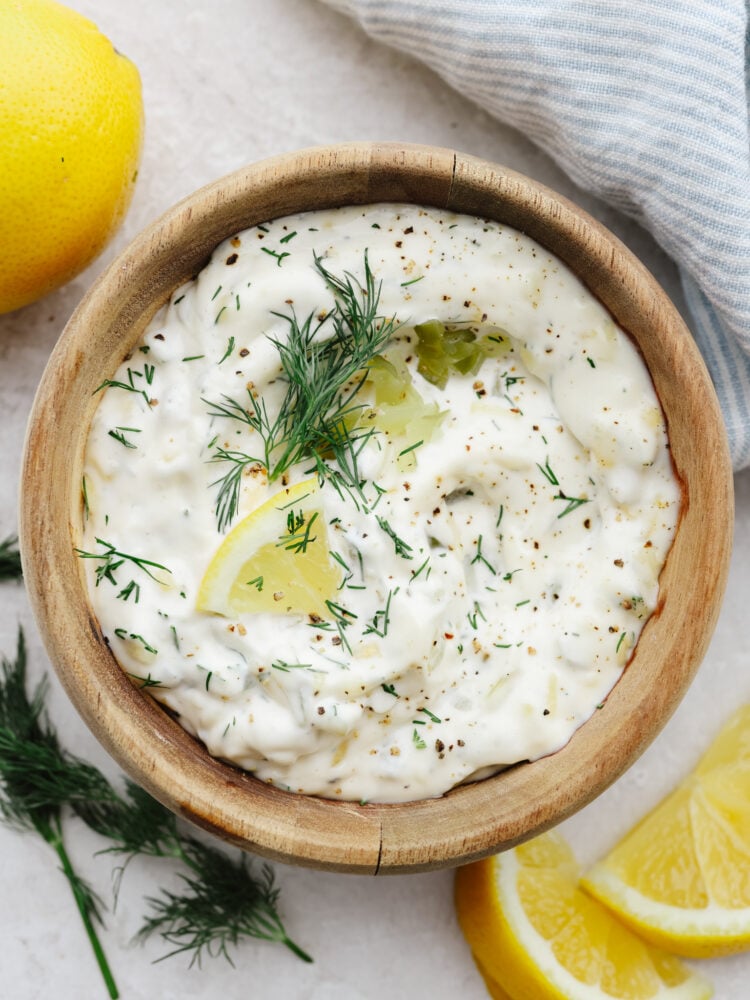 Tartar sauce sprinkled with fresh dill and lemon slices in a wooden bowl. 