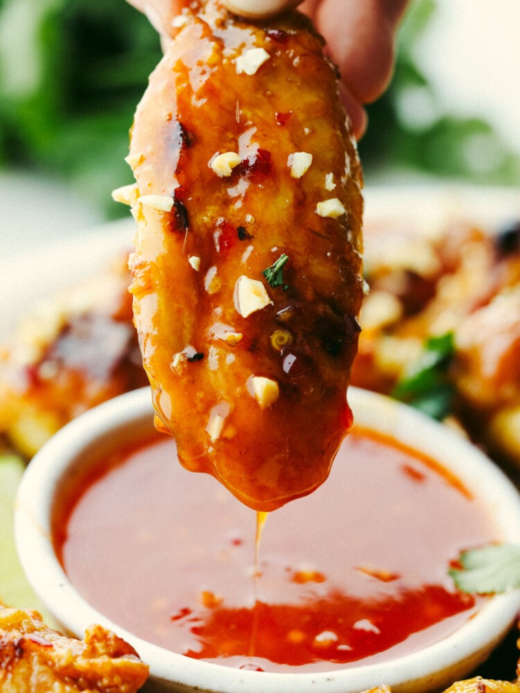 A chicken wing being dipped into Thai sauce. 