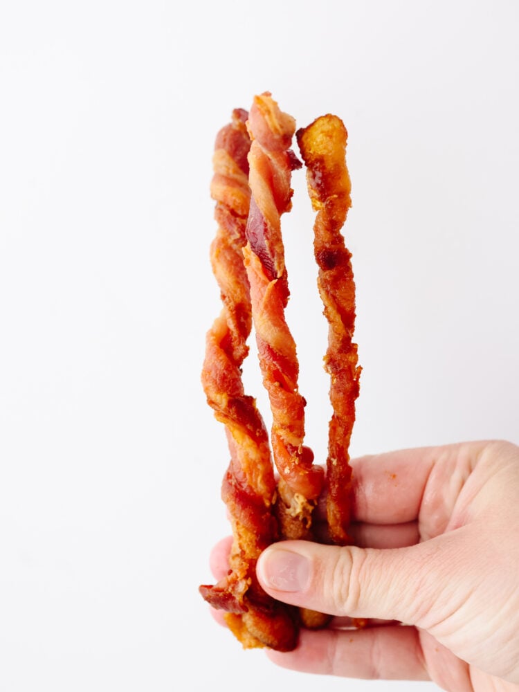 Twisted bacon is beyond easy to make and I love that it's mess-free! Pan-frying bacon can be a little tedious, that's why this method and using an air fryer are my new go-tos! It makes preparing breakfast a breeze. Holding 3 pieces of bacon in-hand.