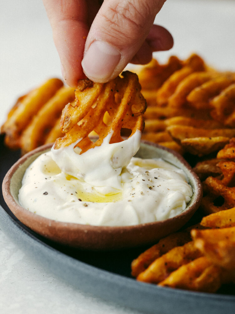 A waffle fry being dipped into garlic aioli sauce. 
