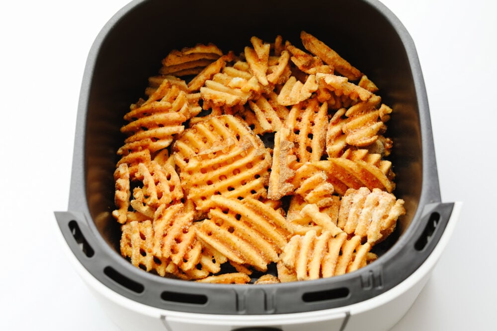 Frozen waffle fries in an air fryer basket. 