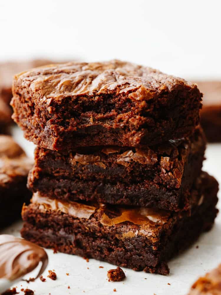 A stack of 3 brownies, one with a bite taken out of it.