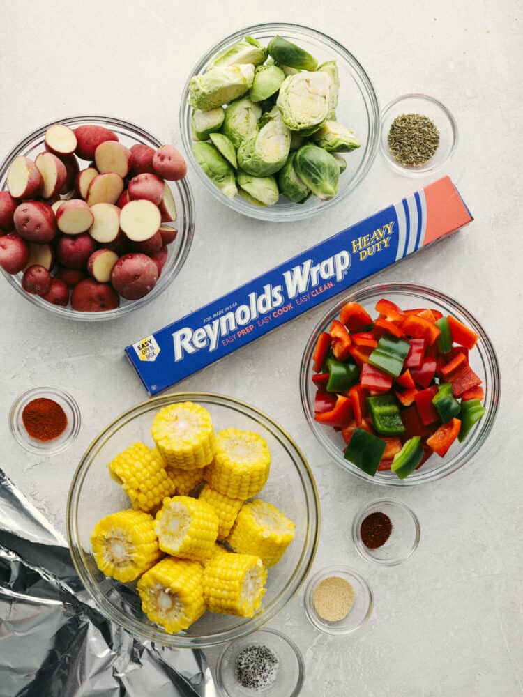 Glass bowls of corn, peppers, potatos and brussel sprouts with a box of Reynolds foil in the middle. 