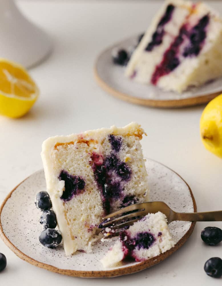 A slice of lemon blueberry cake on a plate with a fork cutting into it. 