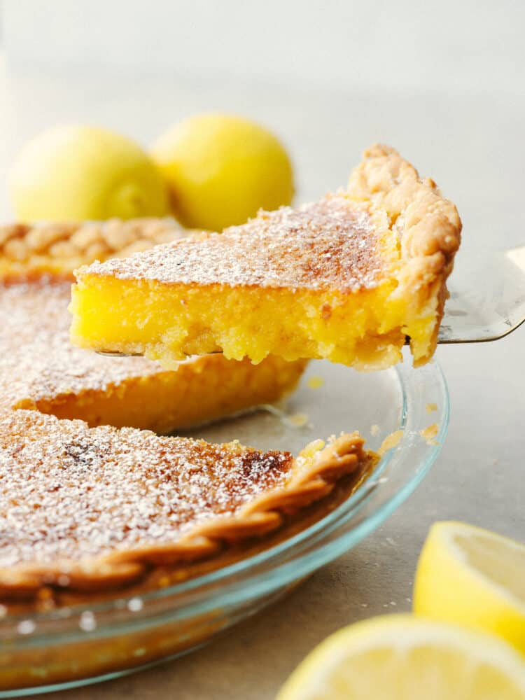 A lemon chess pie with a slice being taken out with a pie server. 