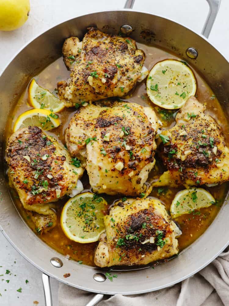 Top-down view of lemon pepper chicken, garnished with lemon, in a metal skillet.