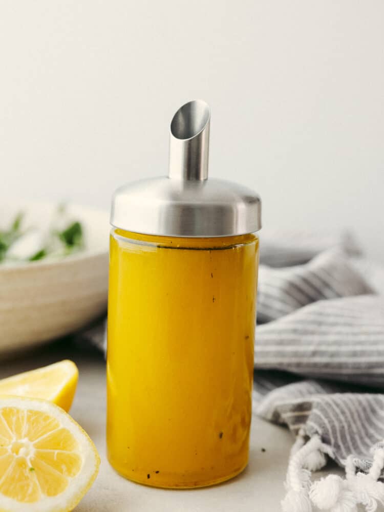 A bottle filled with lemon vinaigrette dressing with a silver pour spout. 