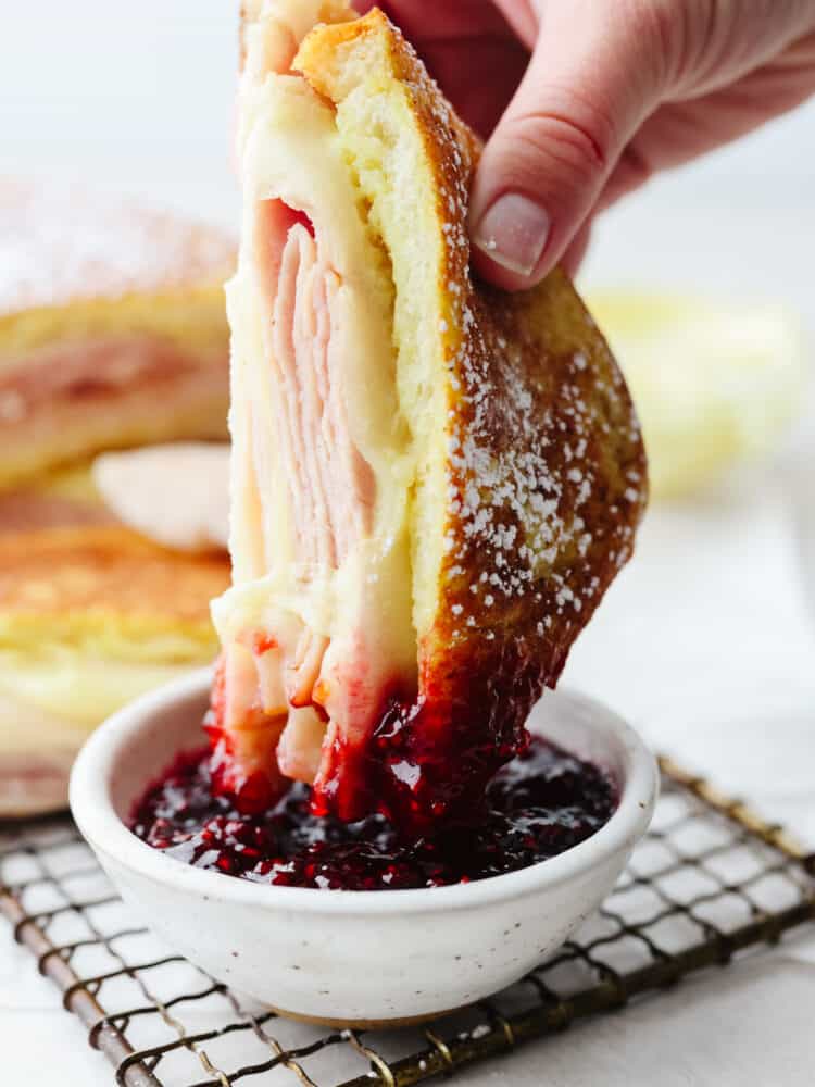 Half of a monte cristo sandwich being dipped into raspberry jam. 