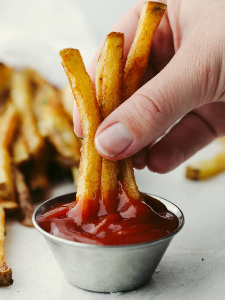 Fries being dipped into ketchup. 