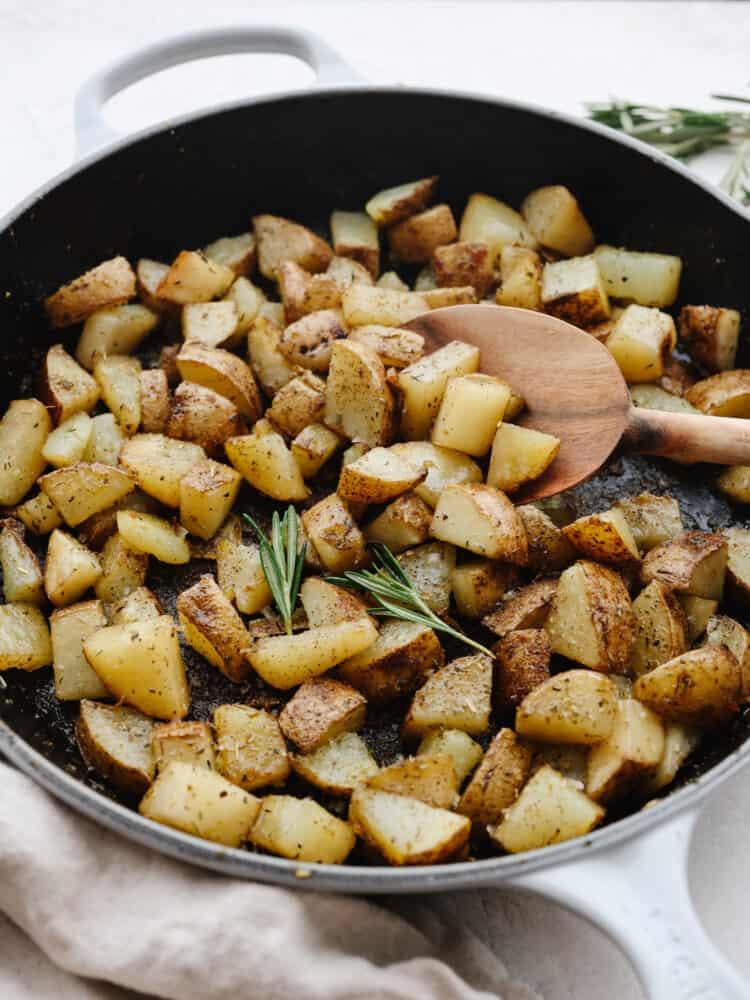 Chopped, cooked potatoes being stirred with a wooden spoon in a shallow skillet.