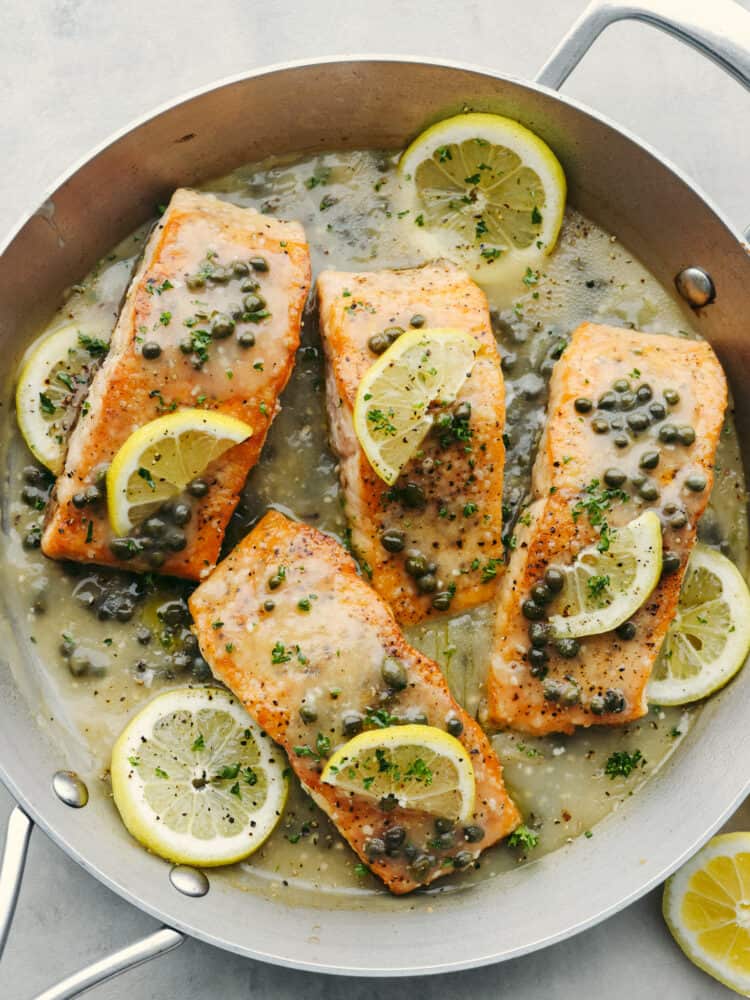 A pan filled witl samon filets covered in lemons and capers. 