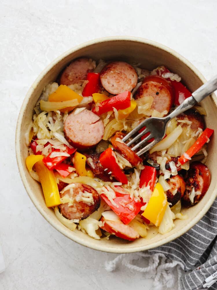 The top view of a bowl filled with kielbasa and sauerkraut and a fork getting a bite. 