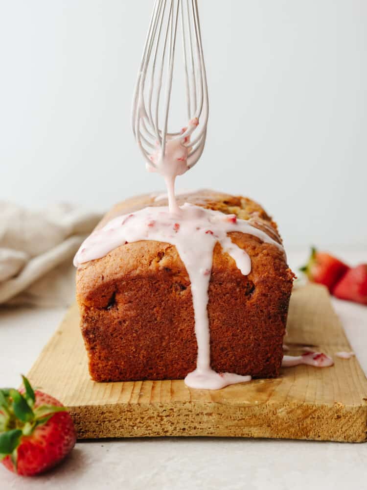A whisk drizzling the strawberry glaze onto the loaf of quickbread. 