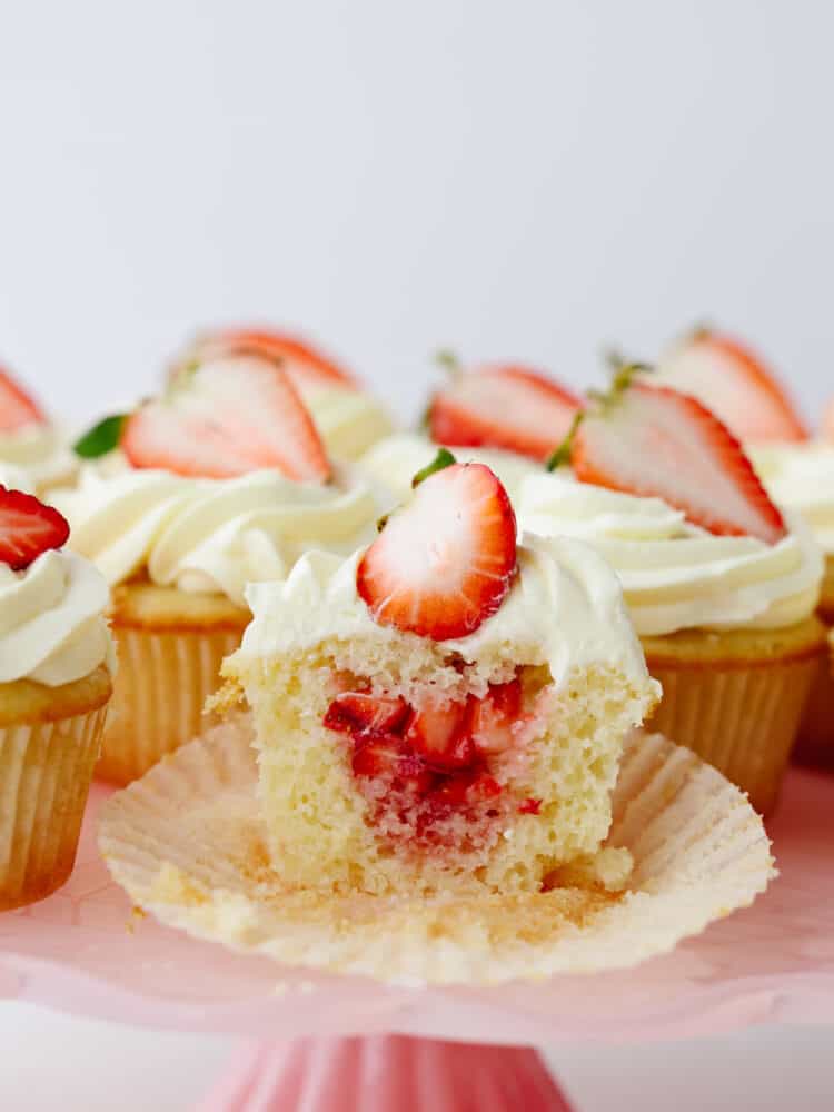 A strawberry shortcake cupcake sliced so that you can see the filling inside. 