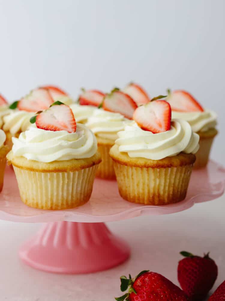 A zoomed in shot of strawberry shortcake cupcake on a pink cake platter. 