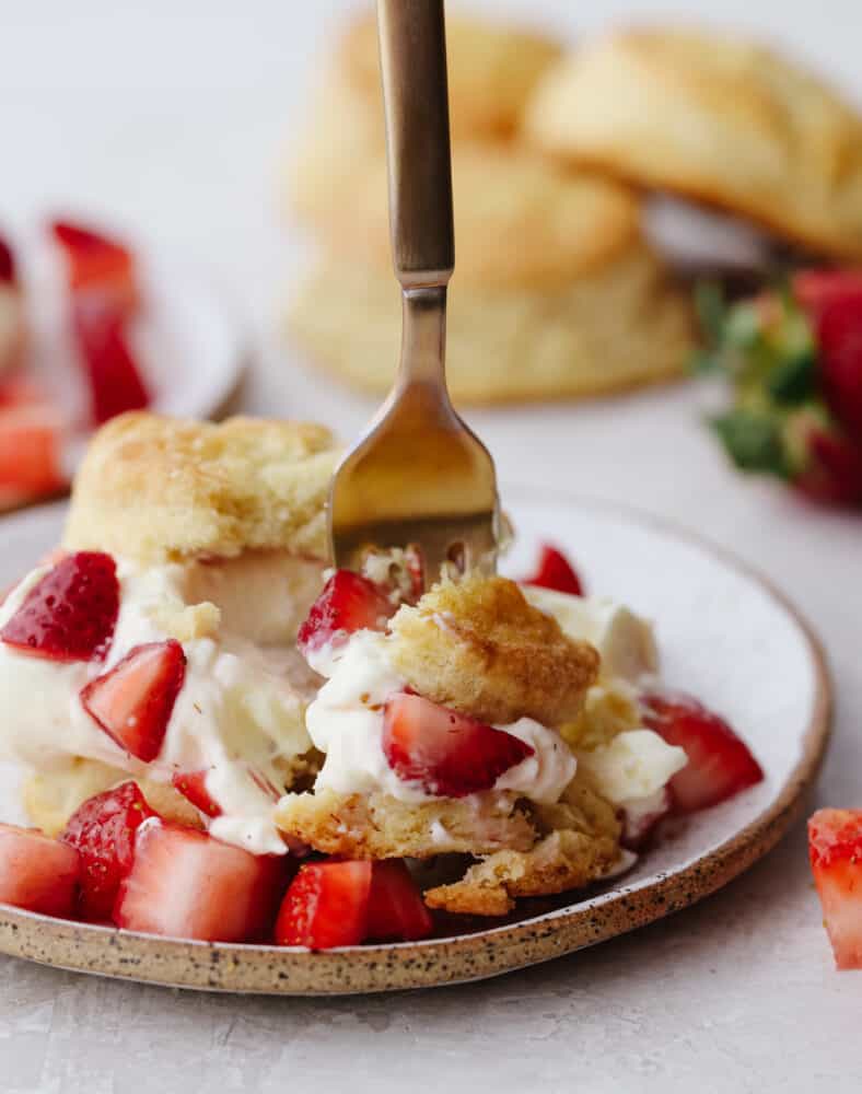 A white speckled plate with strawberry shortcake being scooped up with a silver fork. 