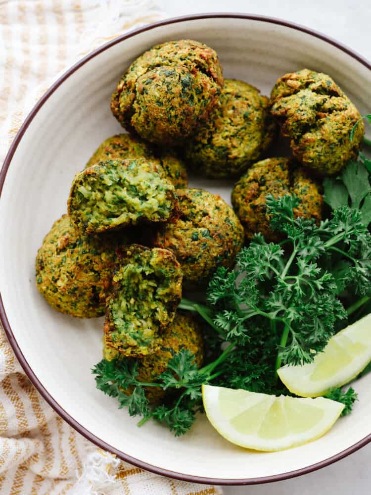 Overhead photo of crispy falafel balls in a bowl and garnished with fresh herbs. 