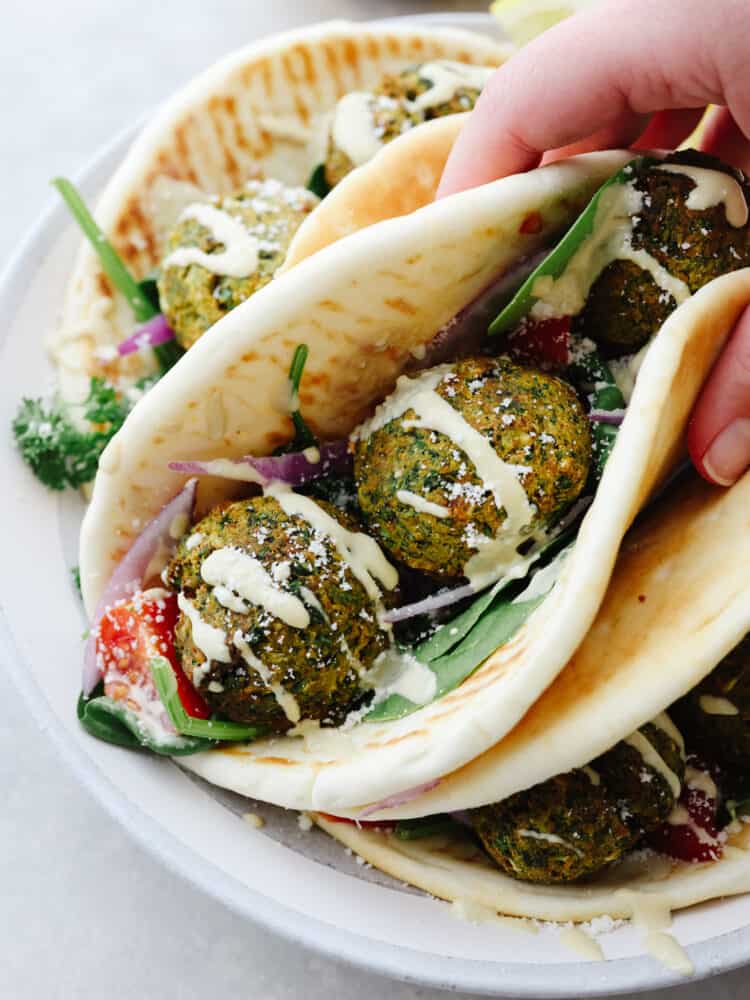 Photo of a handheld wrap. Falafel balls served inside a wrap with lettuce, tomato, and a drizzle of tzaziki sauce.  