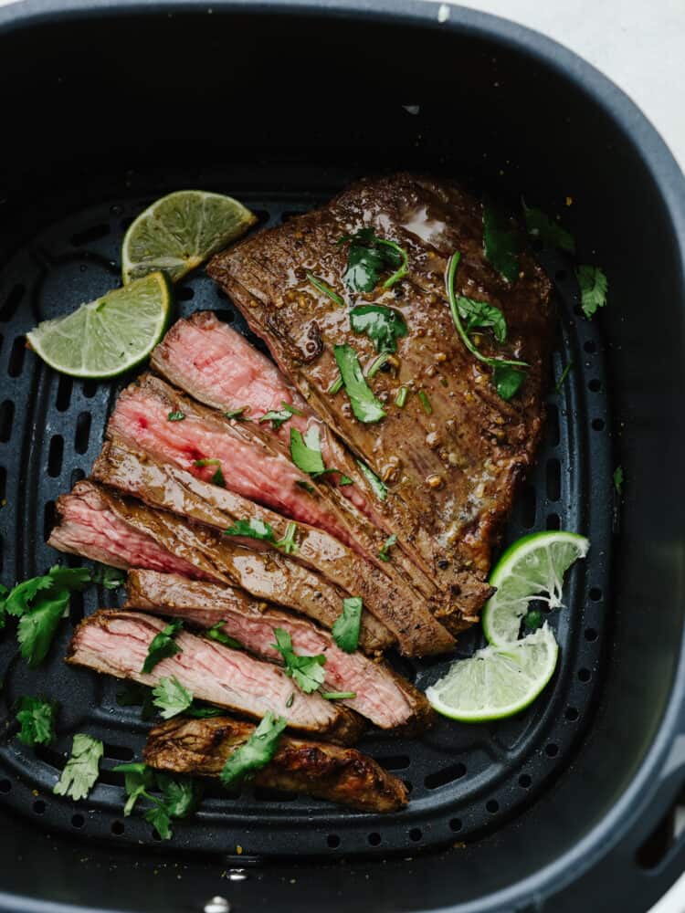 Cooked and sliced flank steak, garnished with lime, in the basket of an air fryer.