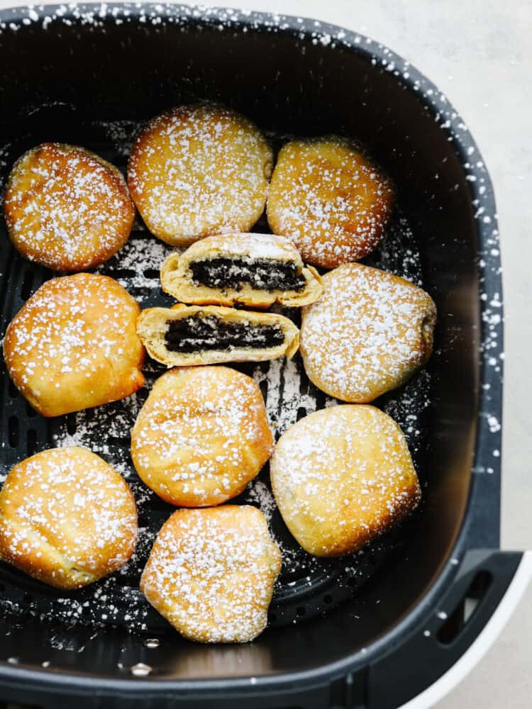 Multiple fried Oreos in the basket of an air fryer, dusted in powdered sugar.