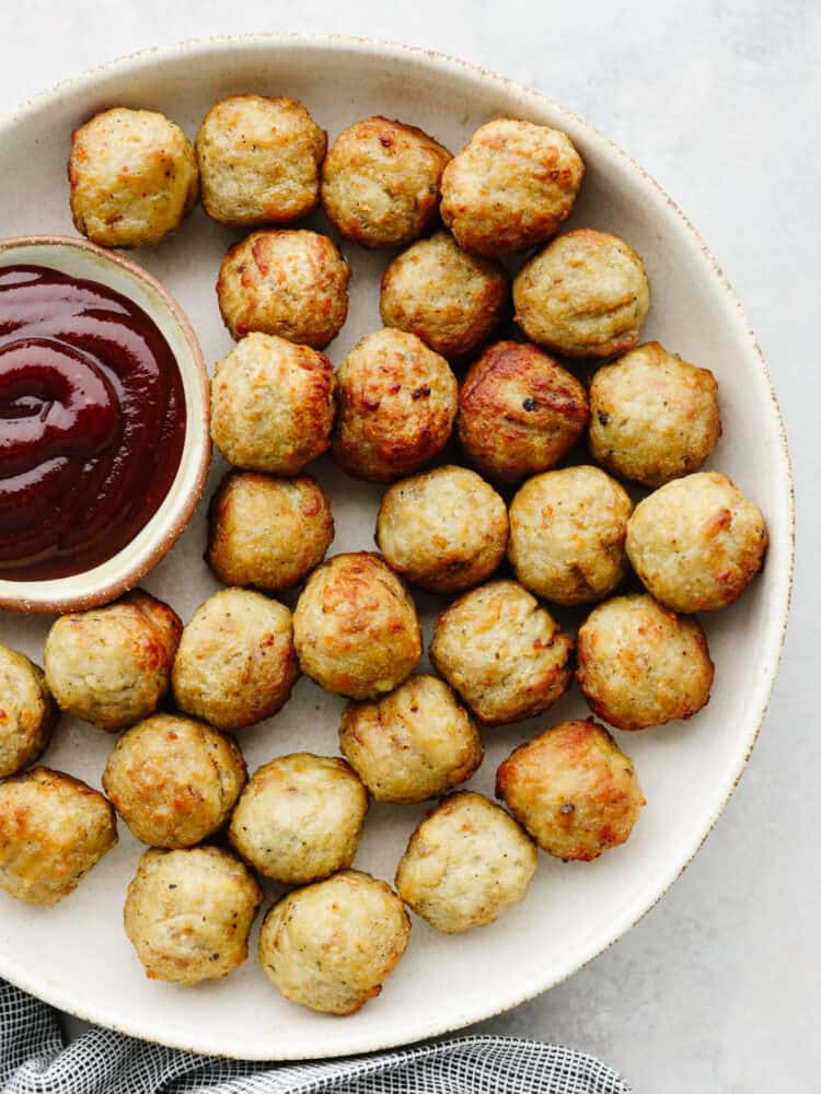 Cooked meatballs on a platter with a small bowl of BBQ sauce on the side. 