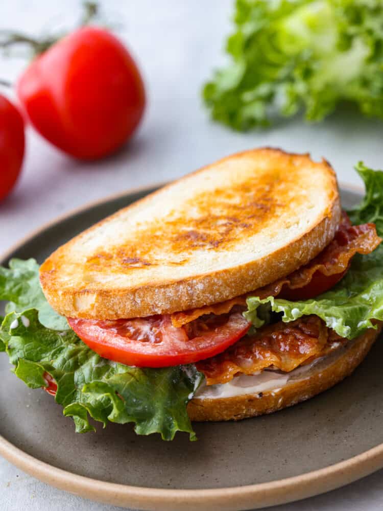 Closeup of a sandwich topped with bacon, lettuce, and tomato on a gray plate.