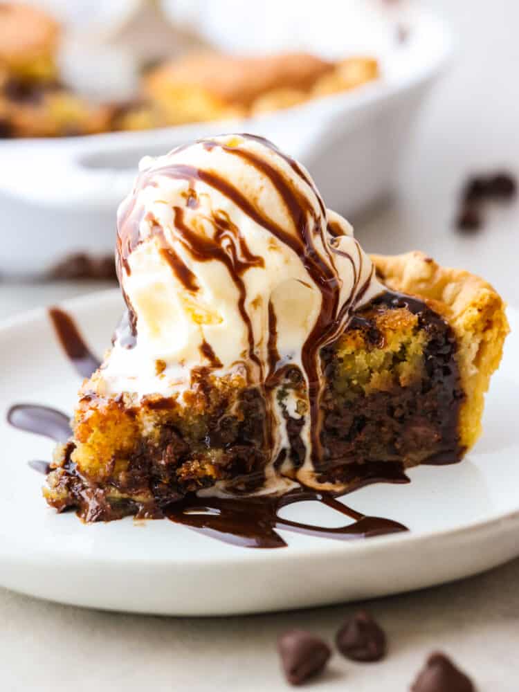 Side view of a chocolate chip cookie pie slice topped with vanilla ice cream and chocolate syrup.