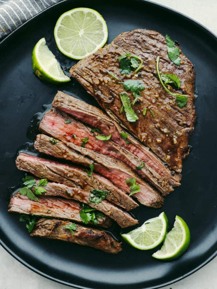 Top-down view of sliced flank steak on a black plate, ready to serve.