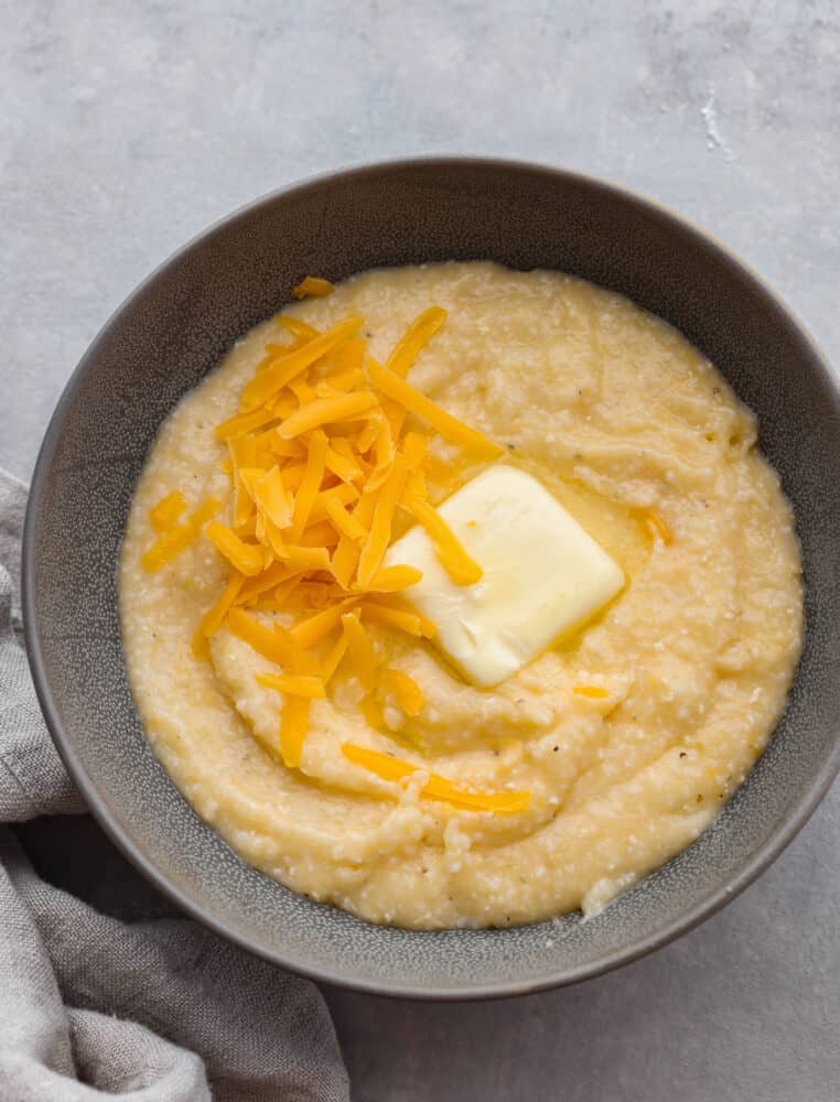 Top view of cheesy grits in a gray bowl.  Garnished with melting butter and shredded cheddar cheese.