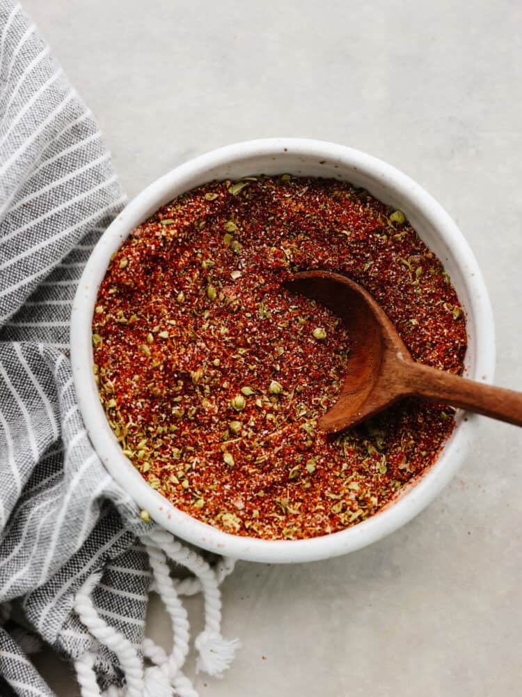 Top-down view of chili seasoning in a white bowl with a wooden spoon in it.