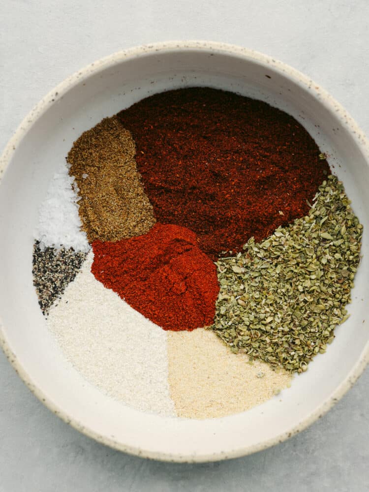 Top-down view of chili seasoning ingredients added to a stoneware bowl.