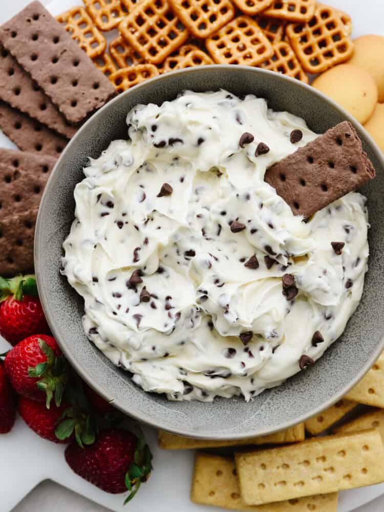 A bowl of chocolate chip cookie dough dip with a chocolate cracker dipped in it. 