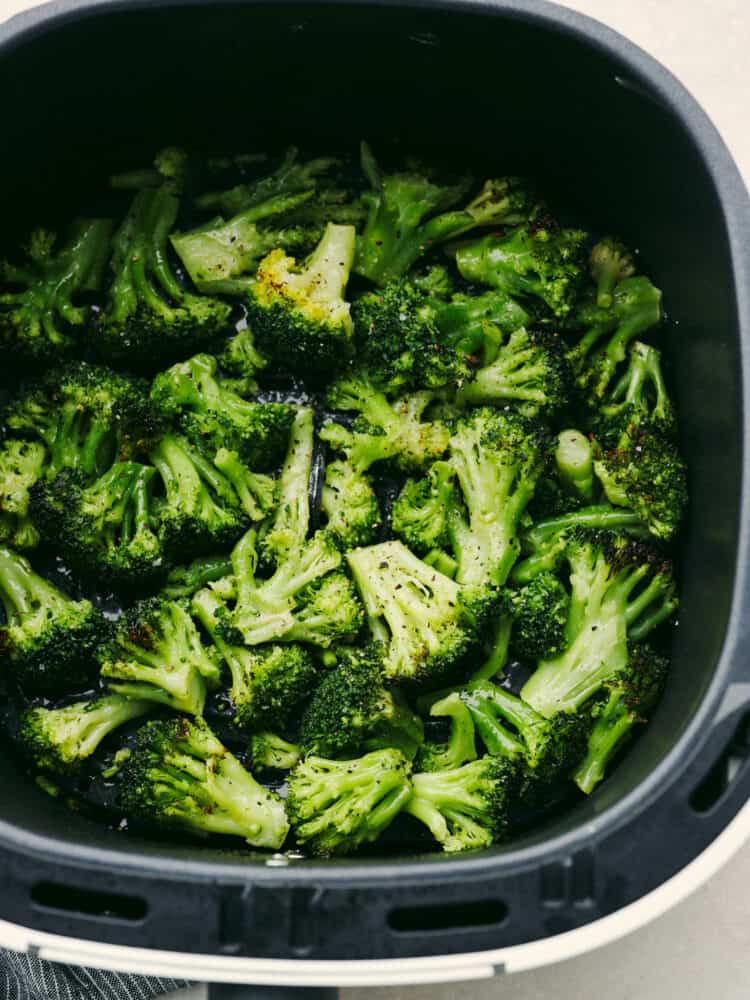 Broccoli in an air fryer basket seasoned with salt and pepper. 