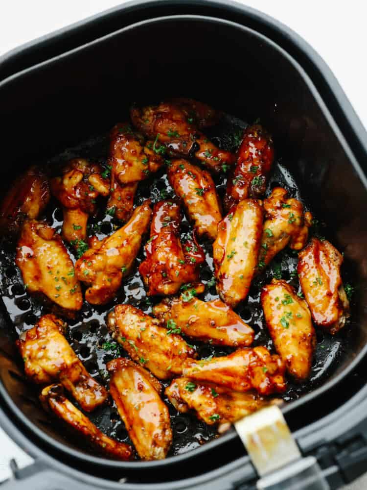 Cooked chicken wings in the basket of an air fryer, tossed in honey buffalo sauce.