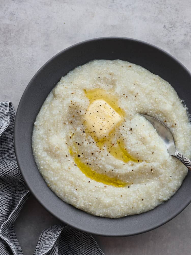 The top view of a bowl of grits with butter and pepper on top. 