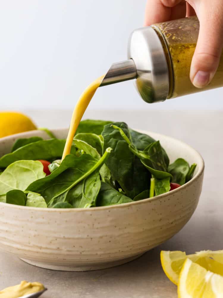 Pouring honey mustard dressing over a green salad in a stoneware bowl.